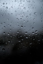 Close-up of raindrops falling softly on a windowpane during a calm evening.
