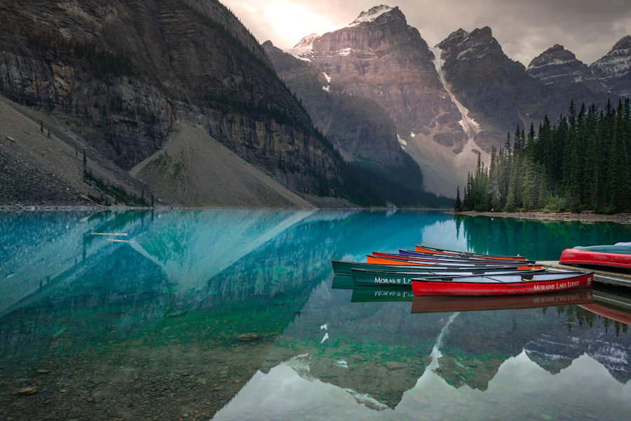 Colourful rental canoes moored at the dock on turquoise Moraine Lake with mountain peaks behind them