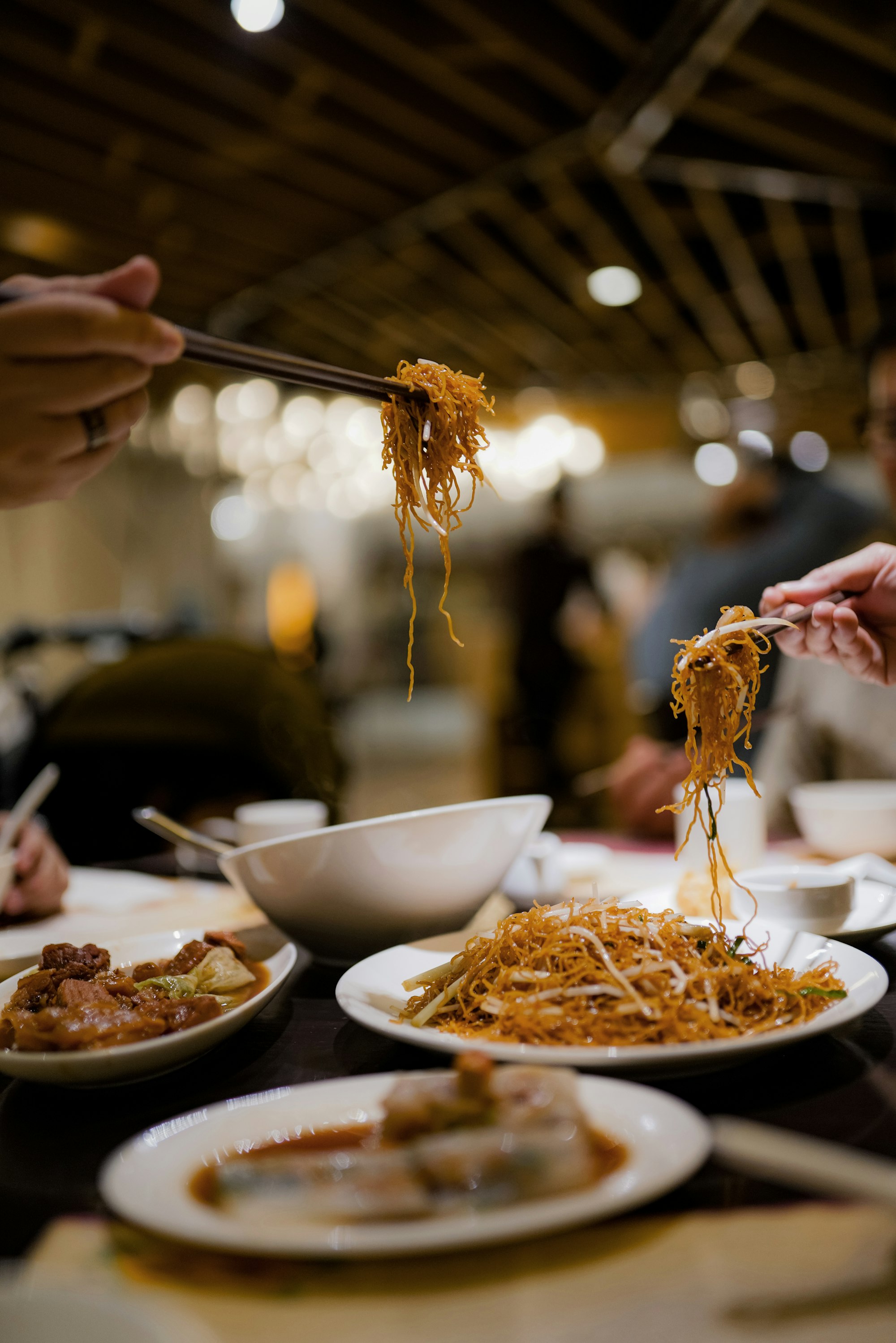 Restaurant guests enjoying Chinese food cuisine with chopsticks and bowls filled with food.