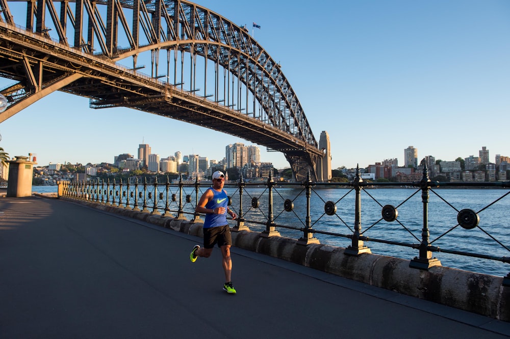 man wearing blue tank top running under bridge