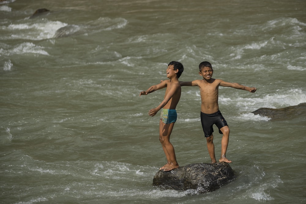 two boys standing on rock in beach