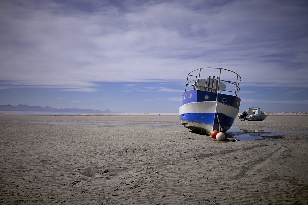 white and blue boat on brown sand during daytime