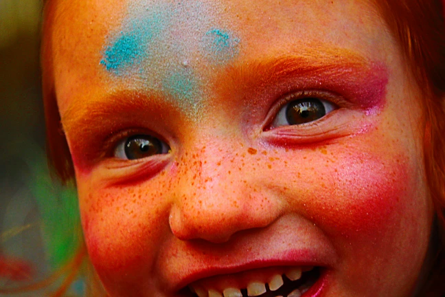 Children laughing as they paint colorful faces at a lively stall.