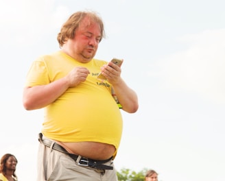 man in yellow shirt and brown pants using smartphone