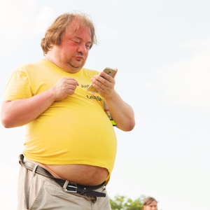 man in yellow shirt and brown pants using smartphone