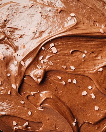 Rich, creamy chocolate spread with a smooth texture is swirled across the surface. Sprinkled lightly are small crystals of salt, contrasting with the glossy sheen of the chocolate.