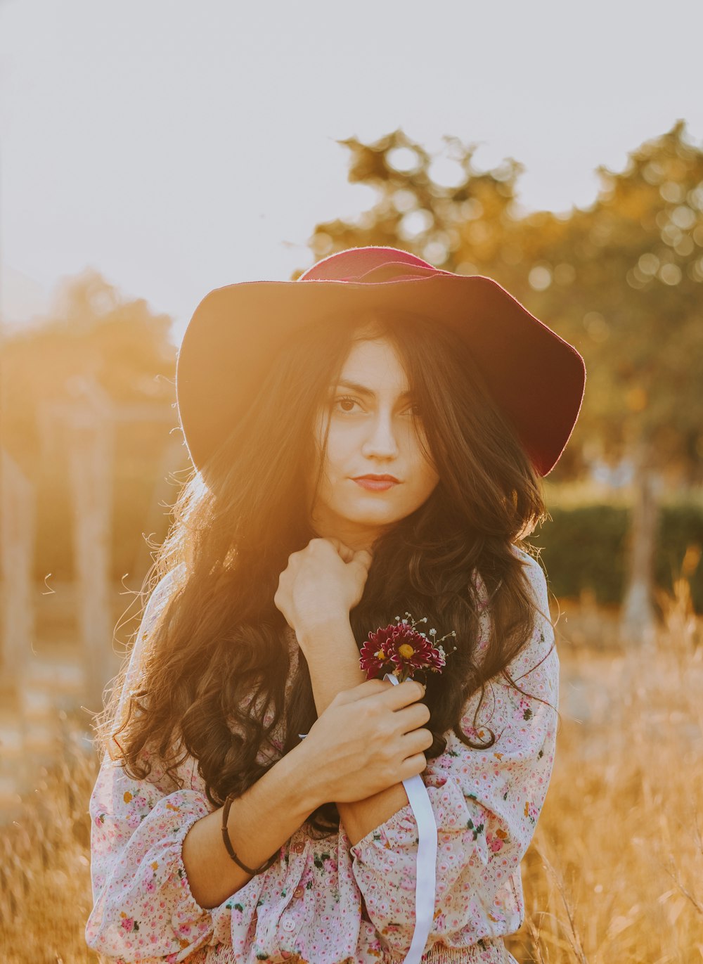 woman in red hat and white floral dress holding flowers