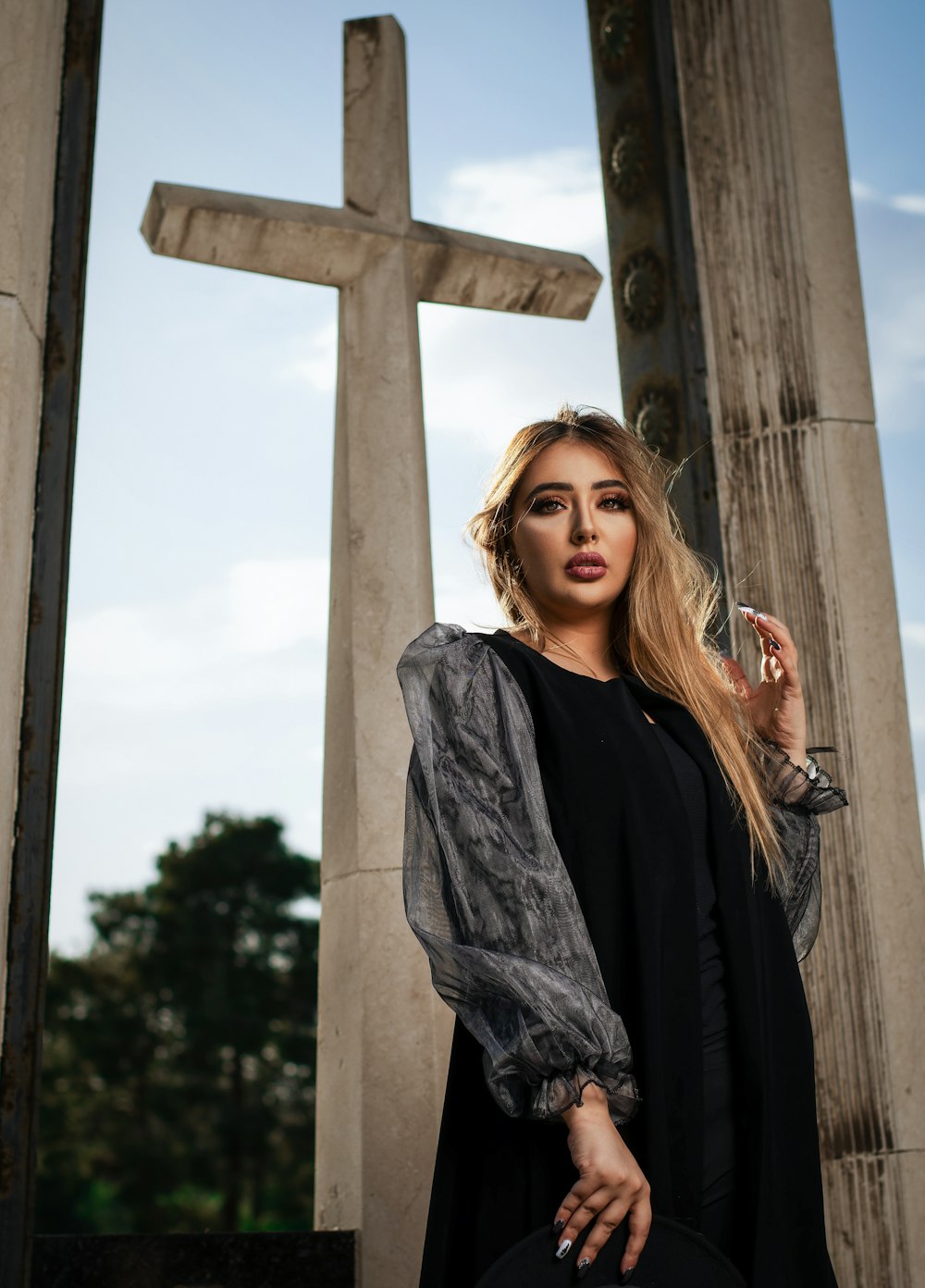 woman in black dress standing near concrete cross