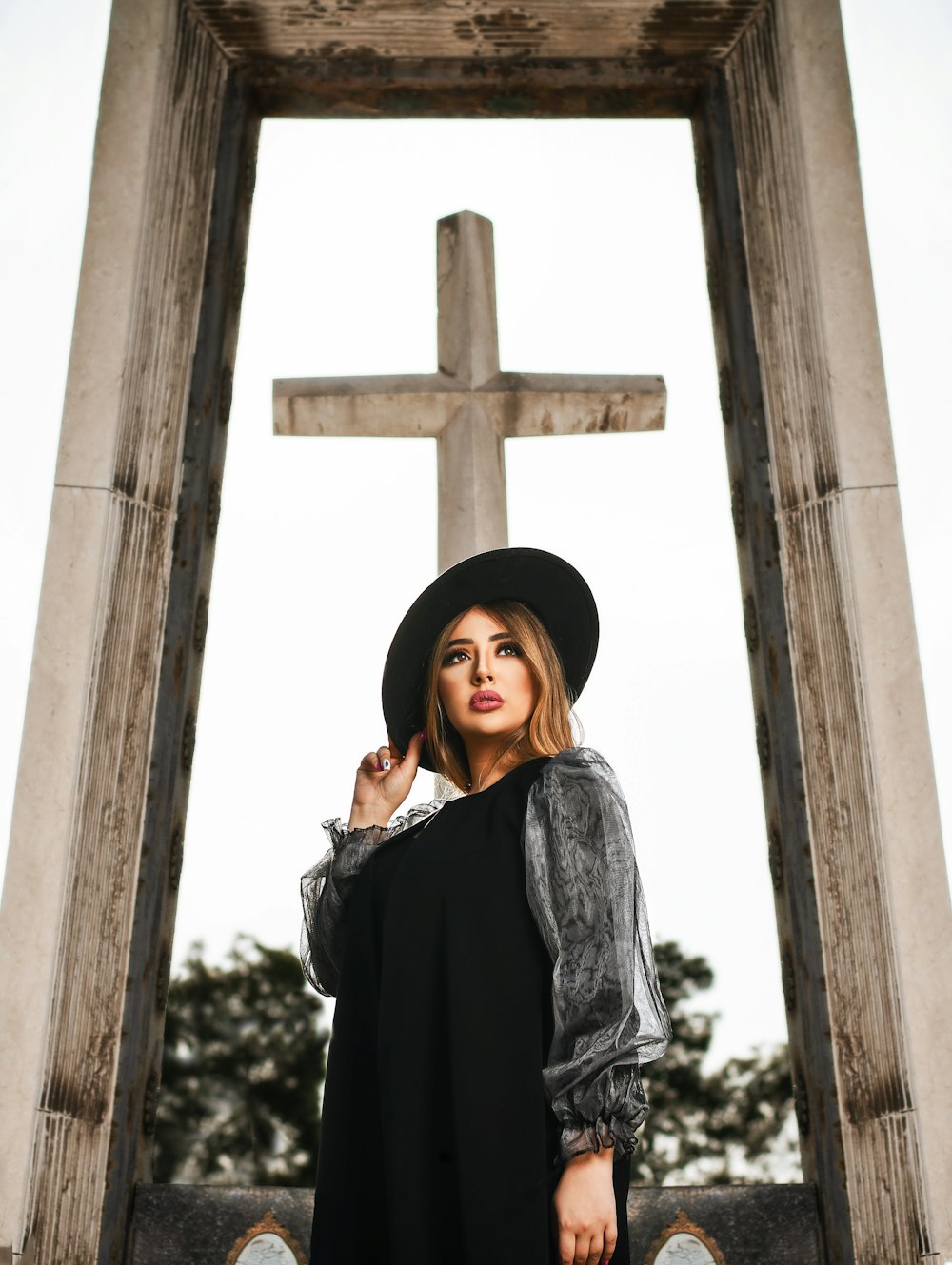woman standing and touching her hat beside brown wooden cross
