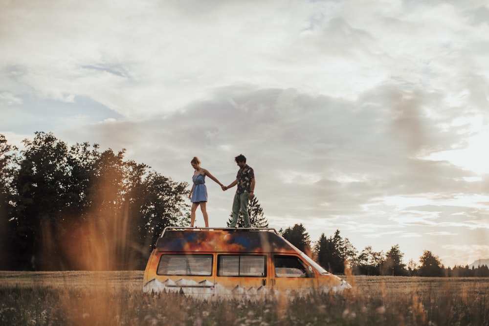 나무 근처 풀밭에 있는 차량 지붕 위에 서 있는 두 명의 여성