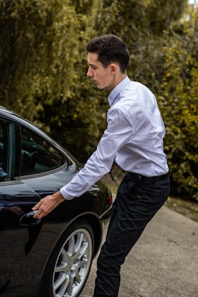 A professional driver opening the car door for a passenger in a sleek black vehicle.