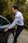 A driver opening a car door for a passenger near a countryside path.