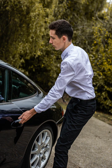 A friendly driver opening the door of a sleek black car at Bergamo airport terminal.