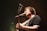 A musician passionately sings into a microphone while playing an acoustic guitar. The stage lighting creates a warm, intimate atmosphere with a slight focus on the musician.