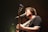A musician passionately sings into a microphone while playing an acoustic guitar. The stage lighting creates a warm, intimate atmosphere with a slight focus on the musician.