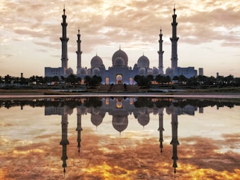 architectural photography,how to photograph majestic reflections of shaik zayed grand mosque and fiery golden sky captured from the oasis of dignity, abu dhabi, uae. 
  
  the oasis of dignity has still water at it's center which gives you splendid reflections of the mosque during mornings and evenings. a good place to find fellow travel & professional photographers clicking those reflections!; white and gray mosque in front of body of water