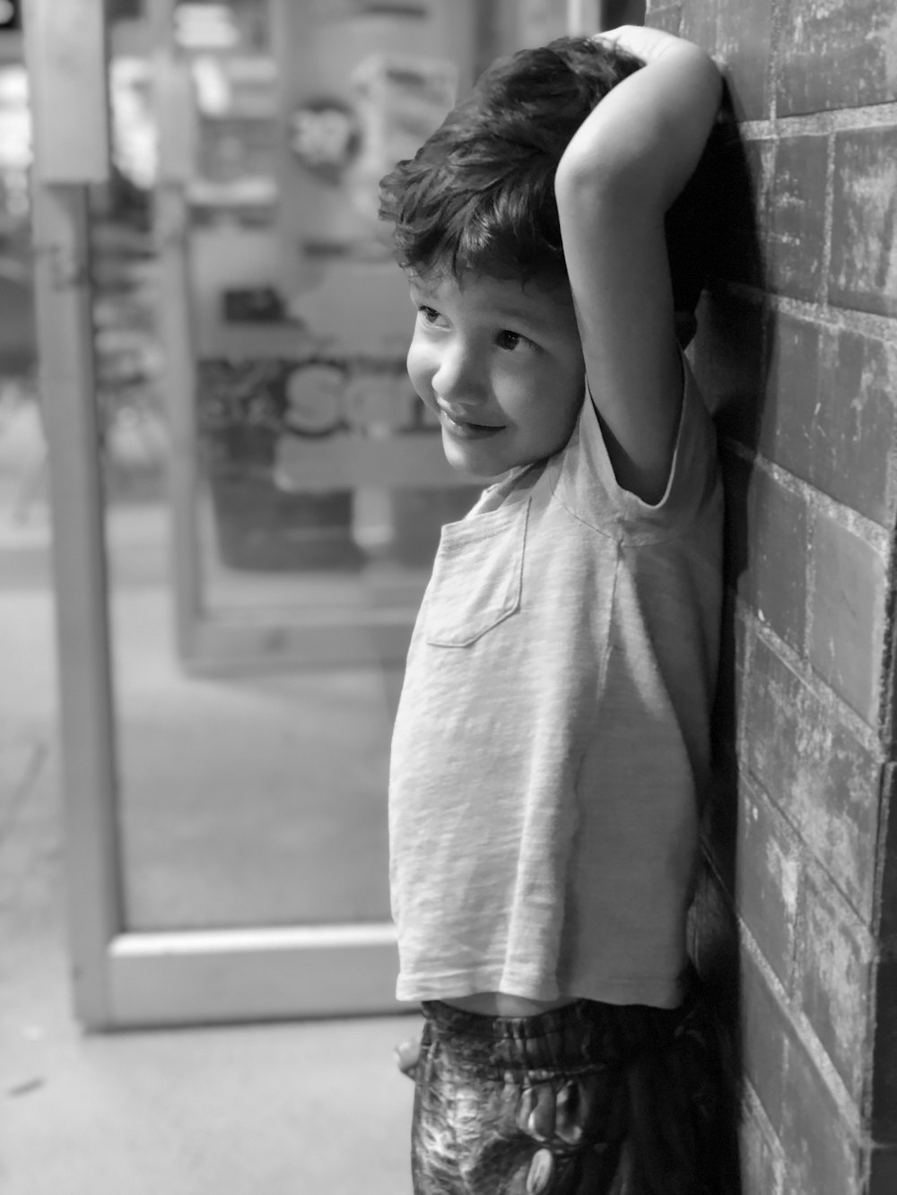 grayscale photo of boy leaning on wall