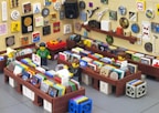 A scene depicting a LEGO brick-built record store with colorful records and artwork on the walls. Three LEGO minifigures are interacting within the store, browsing and discussing the records. The walls are covered with various colorful tiles and artistic designs, giving the store a vibrant and eclectic atmosphere. The store has wooden shelves and displays a vintage vibe with its diverse decor.