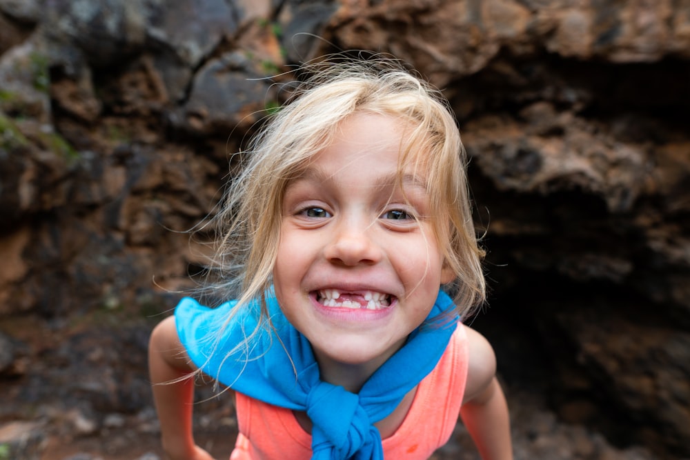 girl standing and smiling near brown rock