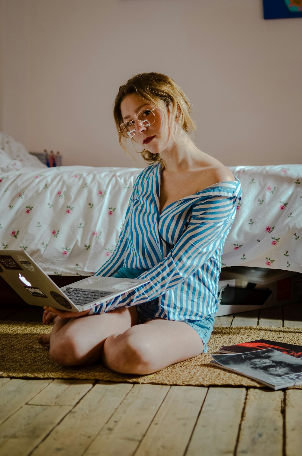 woman in blue and white striped dress shirt and blue denim jeans sitting on floor with laptop computer