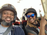Close-up of a passenger holding onto the driver, both wearing casual clothes and helmets.