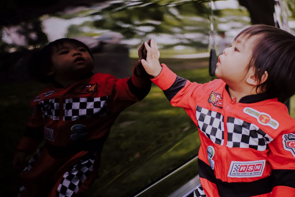 toddler wearing red and black RSN jacket touching black car