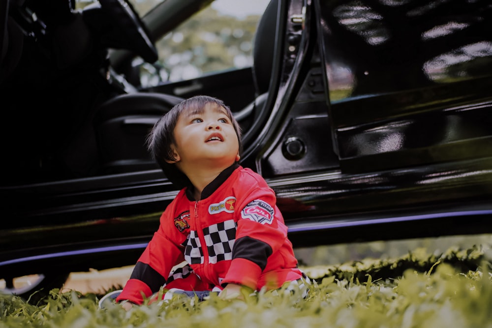 boy sitting on grass in front of parked car