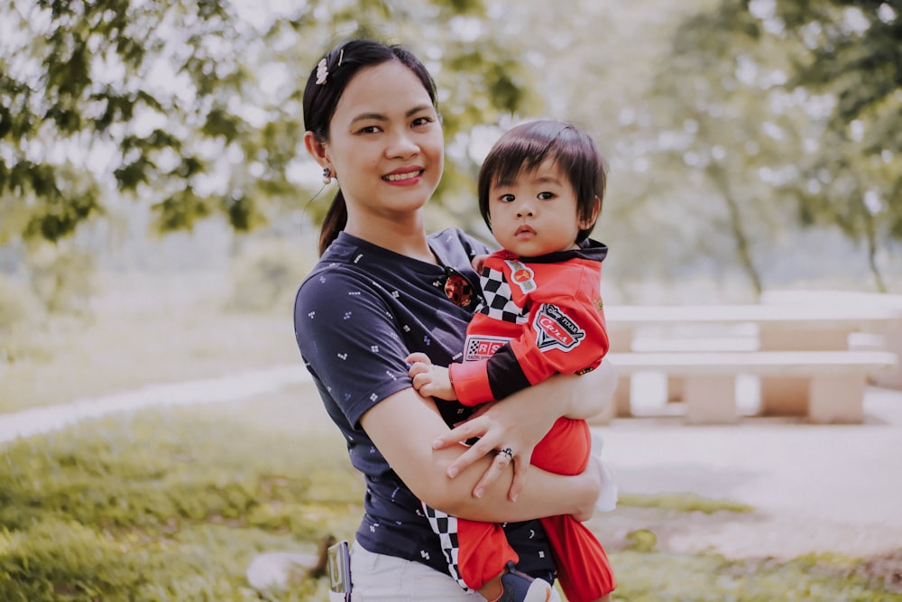 selective focus photography of woman holding toddler in red overalls