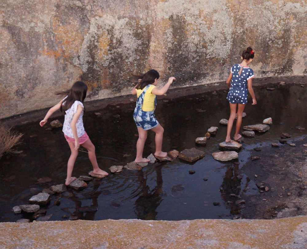 three girls waking on stones between body of water