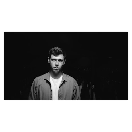 A customer wearing a neutral-toned, contemporary jacket standing against a muted urban backdrop.