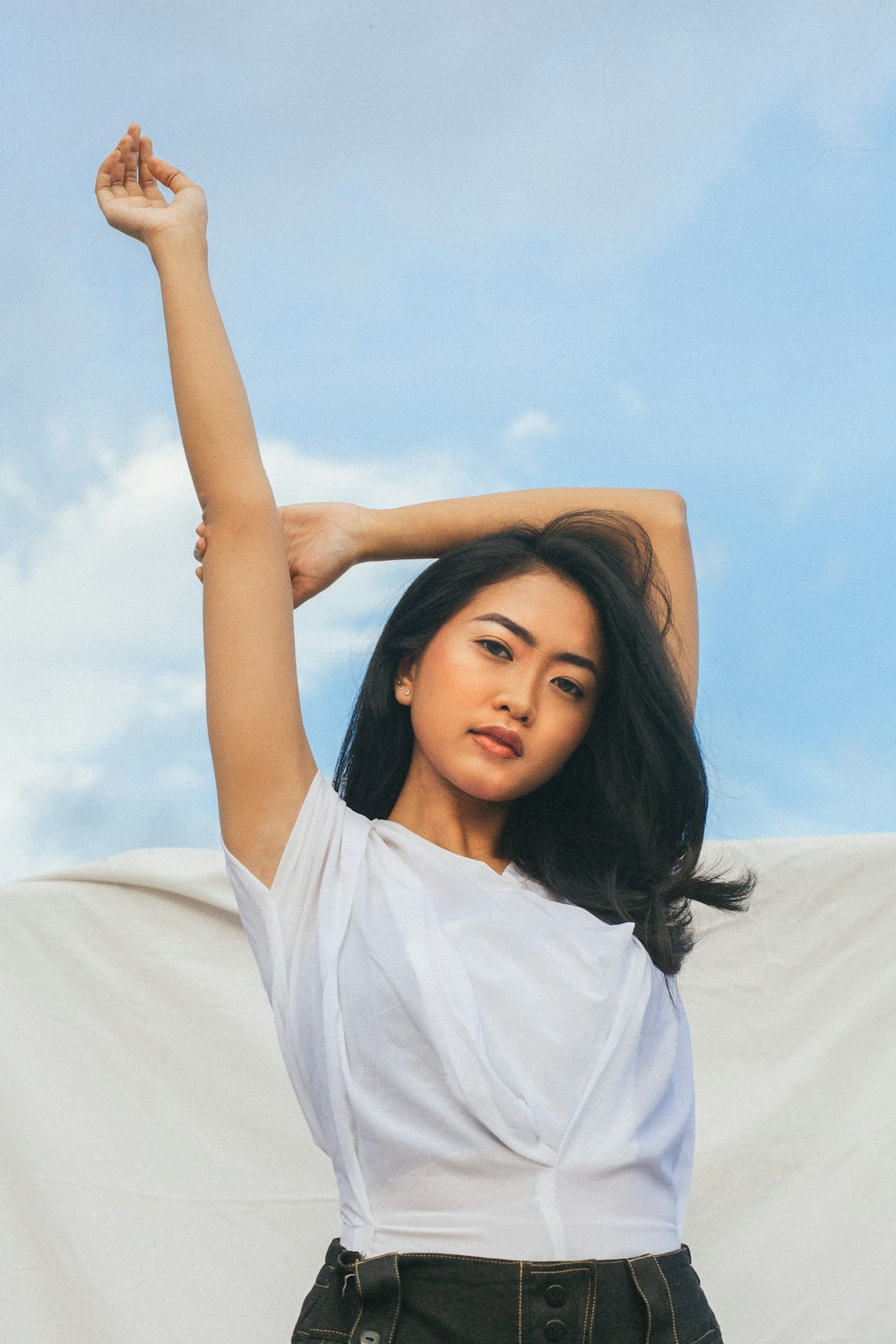 woman in white sleeveless dress posing under cloudy sky