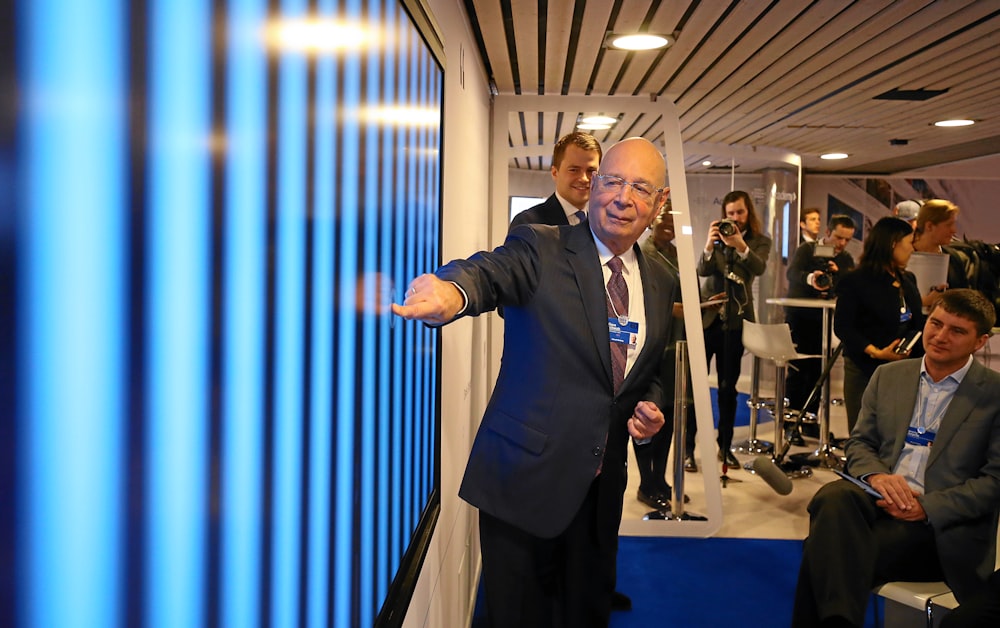 man in black suit pointing in blue screen on wall