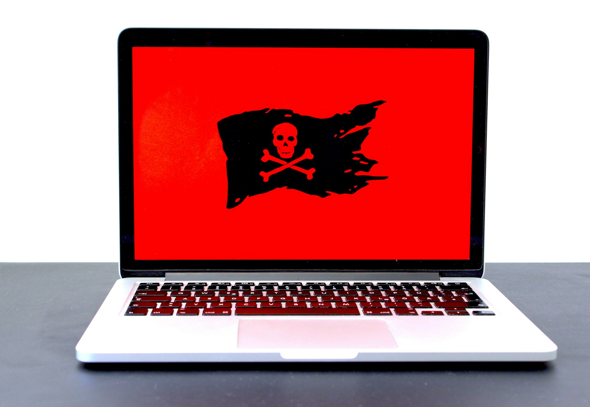 Laptop displaying a pirate flag / jolly roger on a red screen, possibly indicating malware, hackers or a different computer problem.