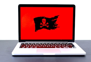 A laptop displaying a red screen with a black pirate flag symbol, featuring a skull and crossbones.