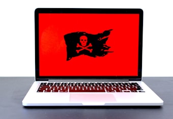 A laptop displaying a red screen with a black pirate flag symbol, featuring a skull and crossbones.