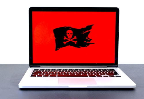 A laptop displaying a red screen with a black pirate flag symbol, featuring a skull and crossbones.