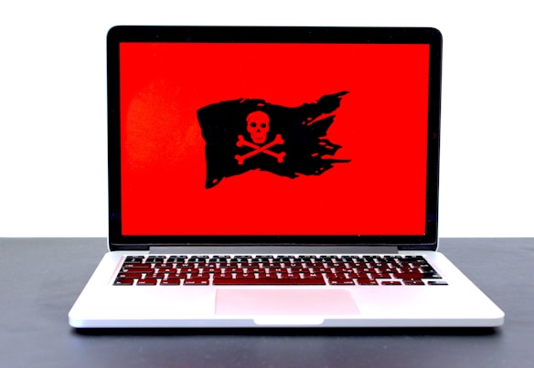 A laptop displaying a red screen with a black pirate flag symbol, featuring a skull and crossbones.