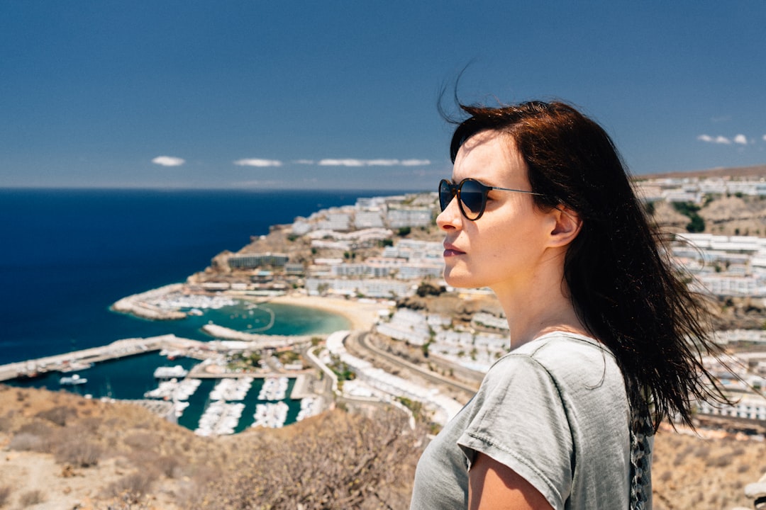 woman in grey t-shirt standing on top of hill overlooking city and sea,