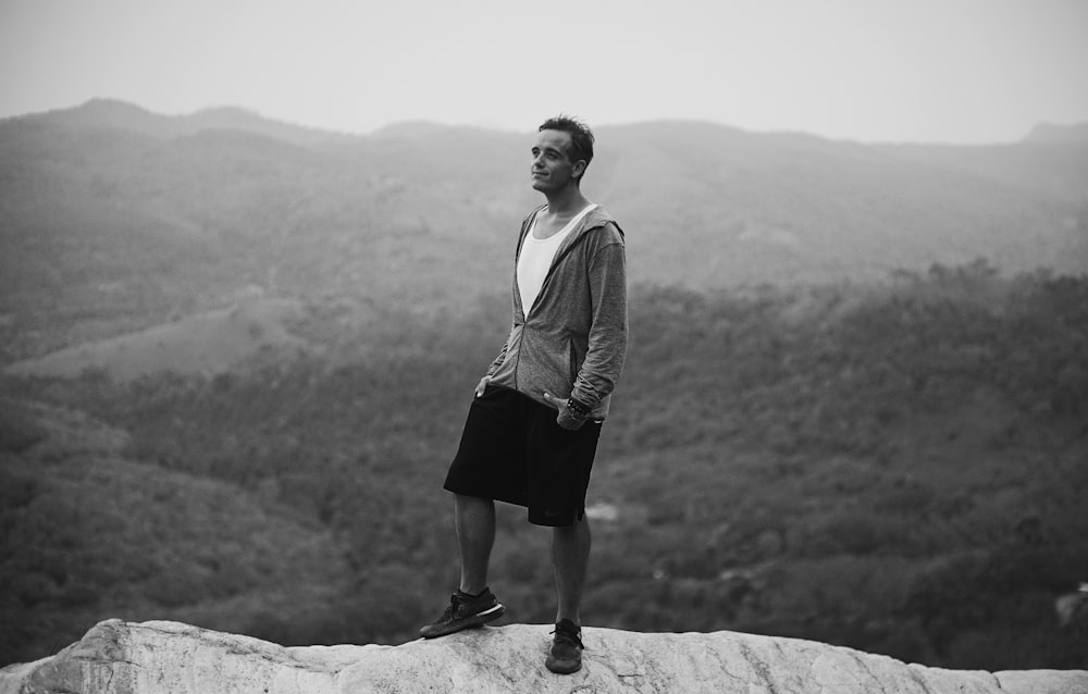 man standing on cliff in grayscale photo