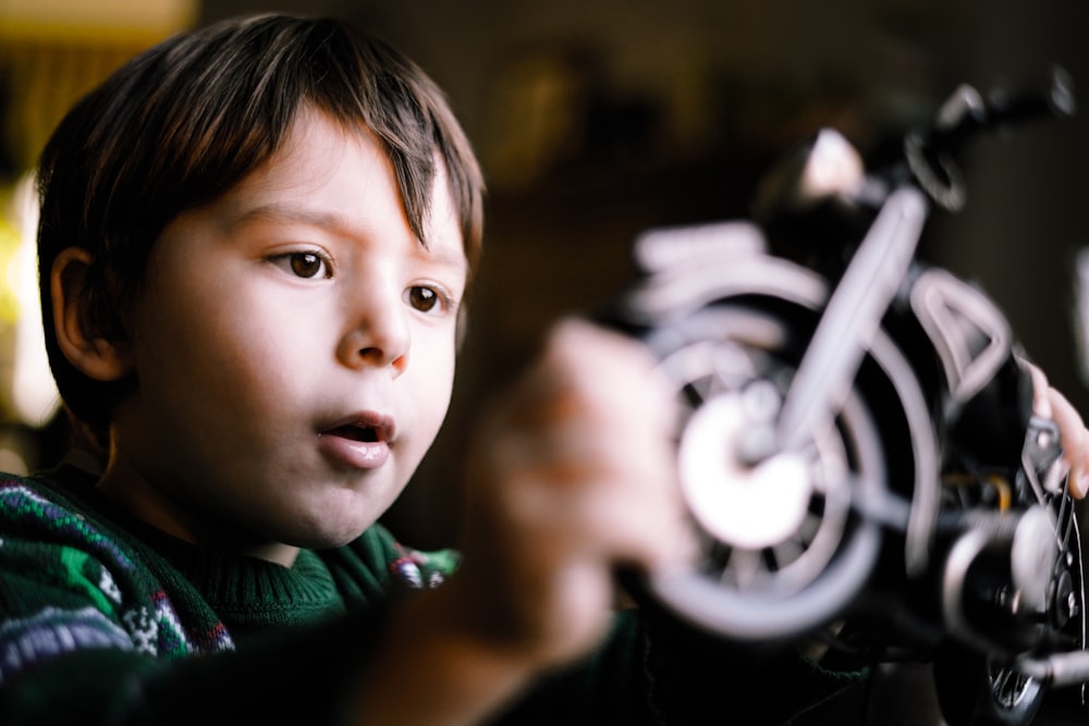 boy wearing green sweater playing with motorcycle toy