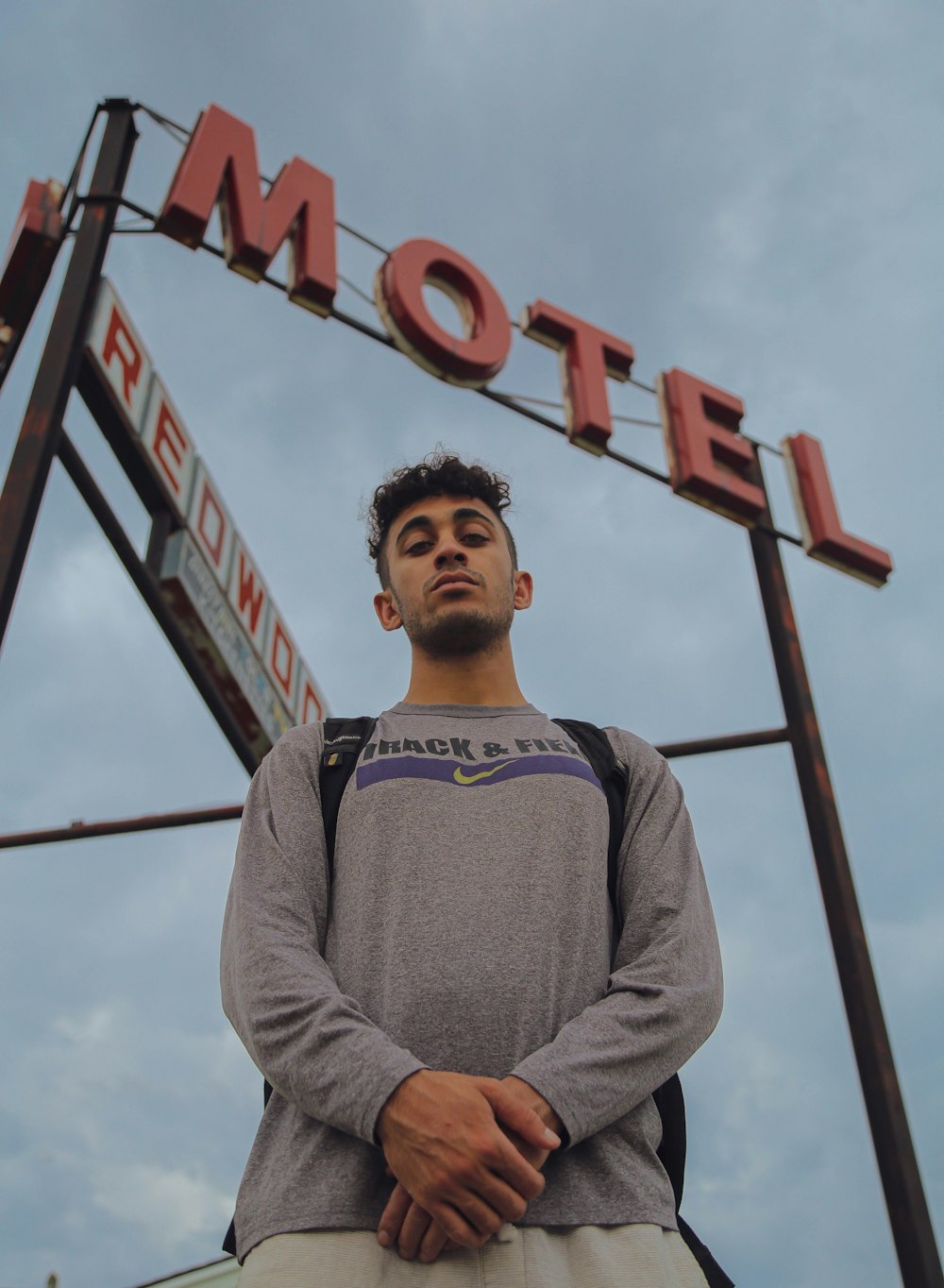 man wearing grey long-sleeved shirt standing beside motel signage