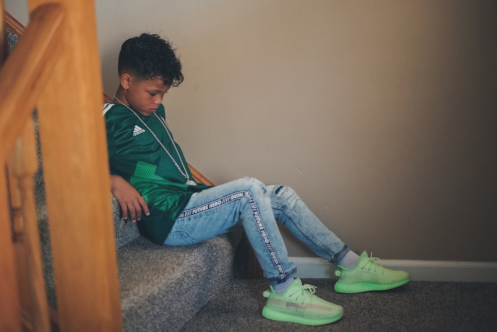 boy in green Adidas shirt sitting on stairs