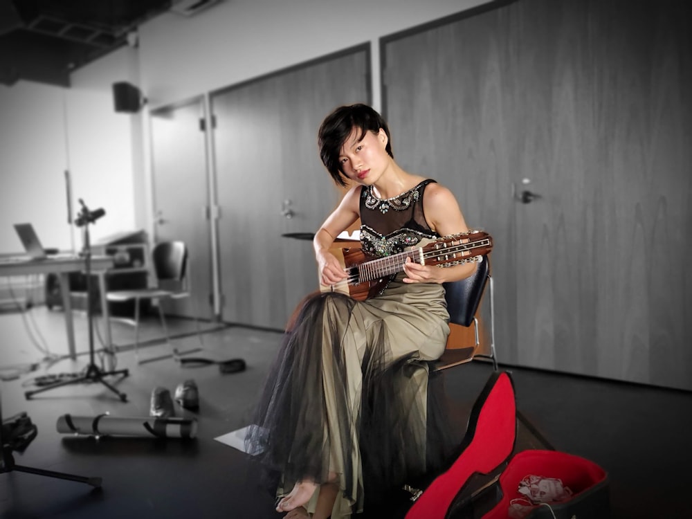 woman wearing gray tank dress holding brown string instrument inside well lit room