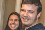 A close-up of two people smiling warmly inside a room, creating a sense of joy and camaraderie. The expressions suggest they are enjoying each other's company and sharing a lighthearted moment.