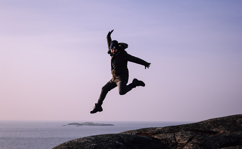 man jumping near cliff during daytime