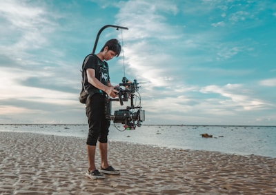 A behind-the-scenes shot of a travel influencer setting up a camera on a sandy beach.