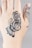 A close-up of a hand with intricate black henna designs covering the skin. The pattern features swirling lines and a butterfly motif, combined with abstract shapes extending to the fingers.