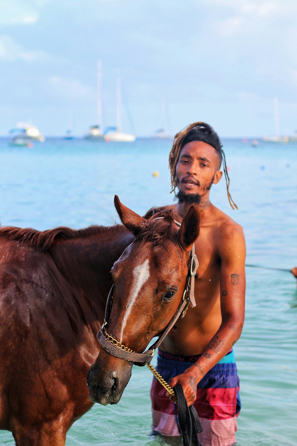 man standing on seashore with brown horse