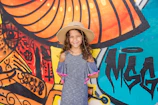 A smiling young girl in a colorful, comfortable dress standing against a vibrant mural.