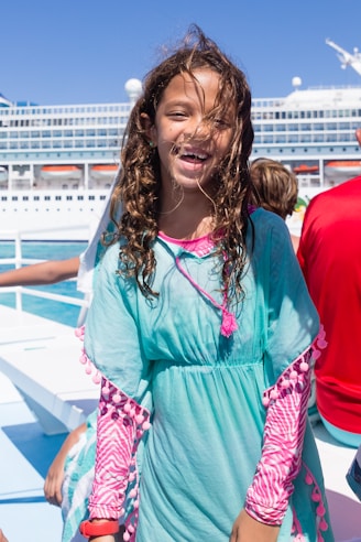 A cheerful travel expert smiling warmly with a backdrop of a sunny beach and cruise ship.